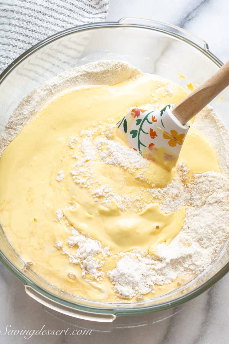 a mixing bowl with a spatula stirring a flour mixture into batter