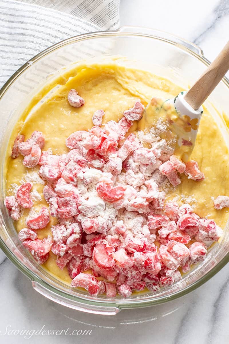 cake batter in a bowl with sliced rhubarb being stirred in