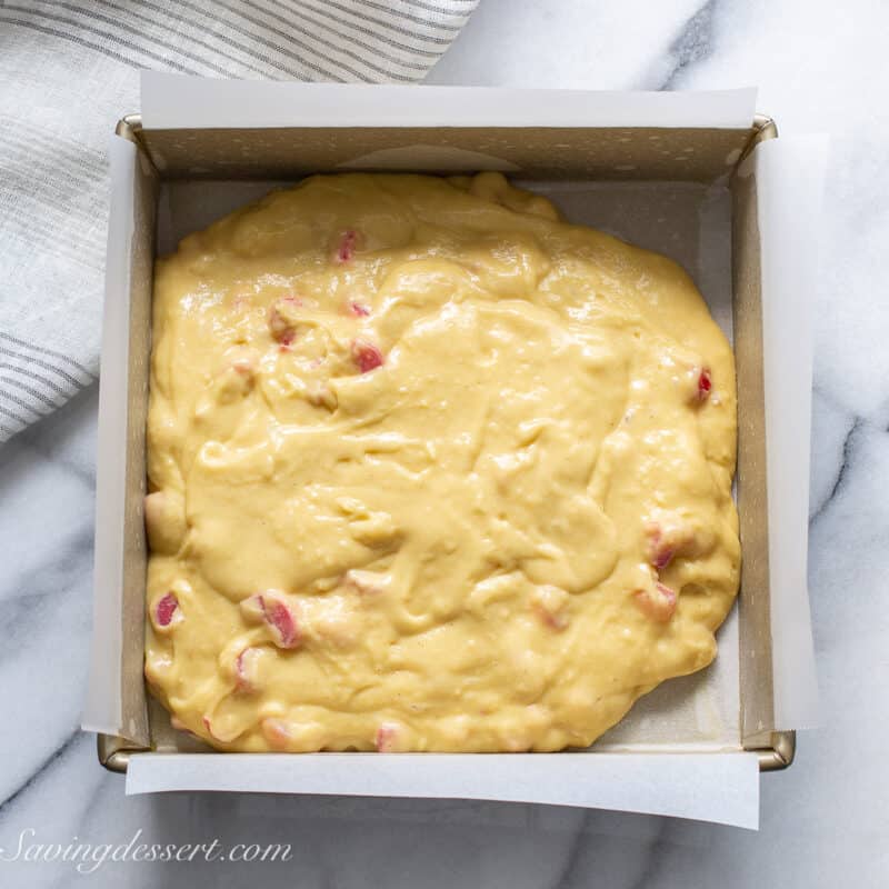 rhubarb cake batter being spread in a square cake pan