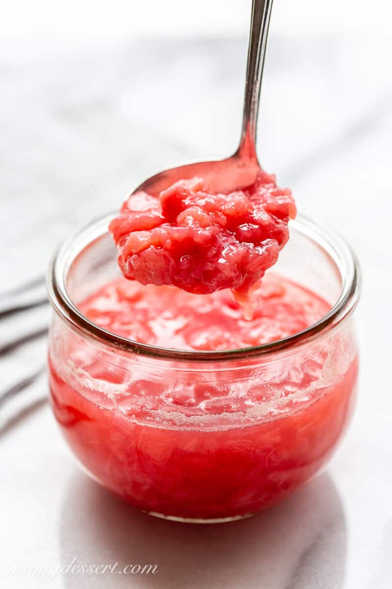 a jar of rhubarb sauce with a ladle scooping out the chunky sauce