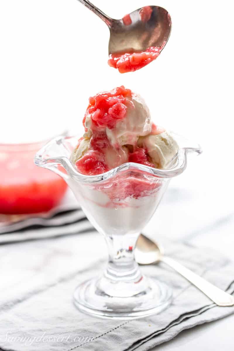 A bowl of vanilla ice cream with rhubarb sauce being poured over the top