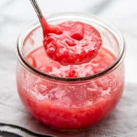 A jar with homemade rhubarb sauce with a ladle scooping out some sauce.