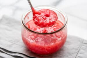 A jar with homemade rhubarb sauce with a ladle scooping out some sauce.