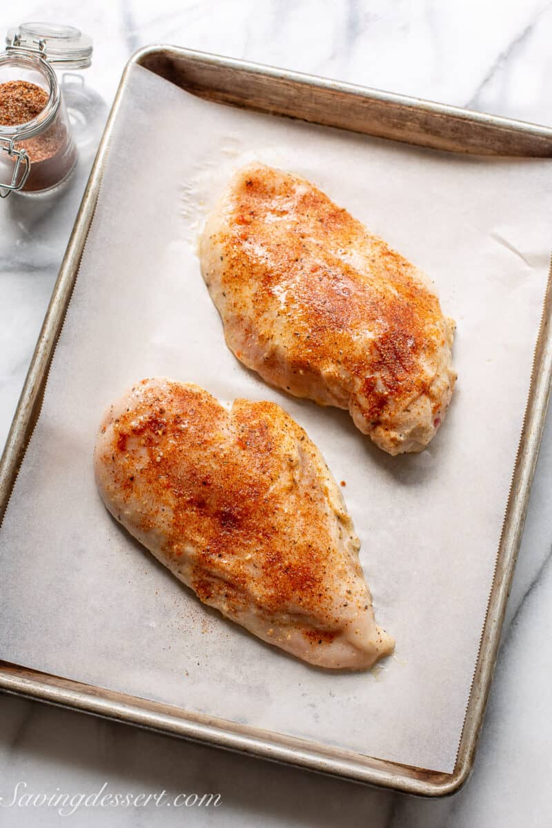 raw chicken breasts sprinkled with rotisserie seasoning on a tray