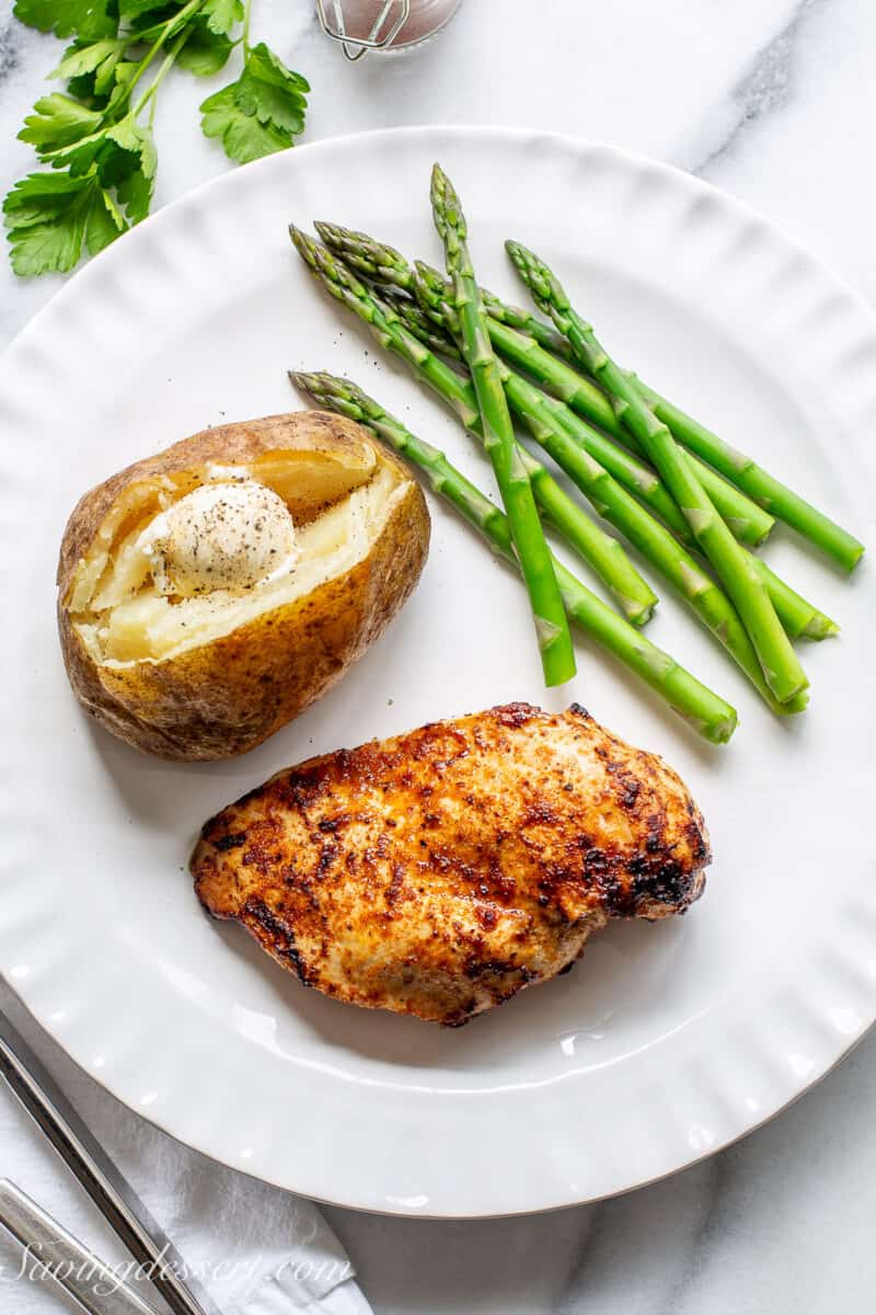 a boneless chicken breast on a plate with a baked potato and asparagus