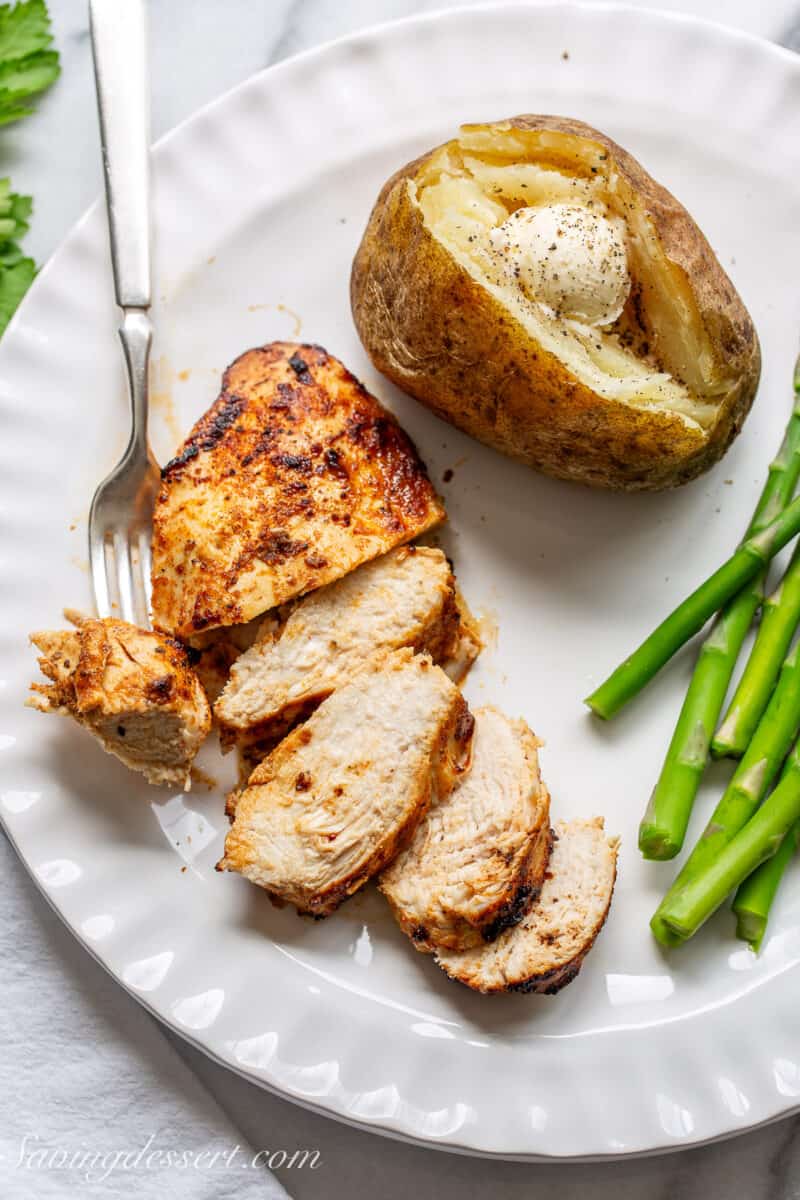 sliced air fryer chicken breast on a plate with a baked potato and asparagus