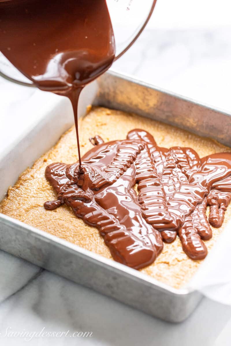 a pan of peanut butter filling being drizzled with melted chocolate