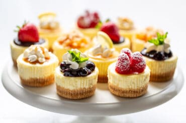 a cake plate covered with individual mini cheesecakes with various toppings