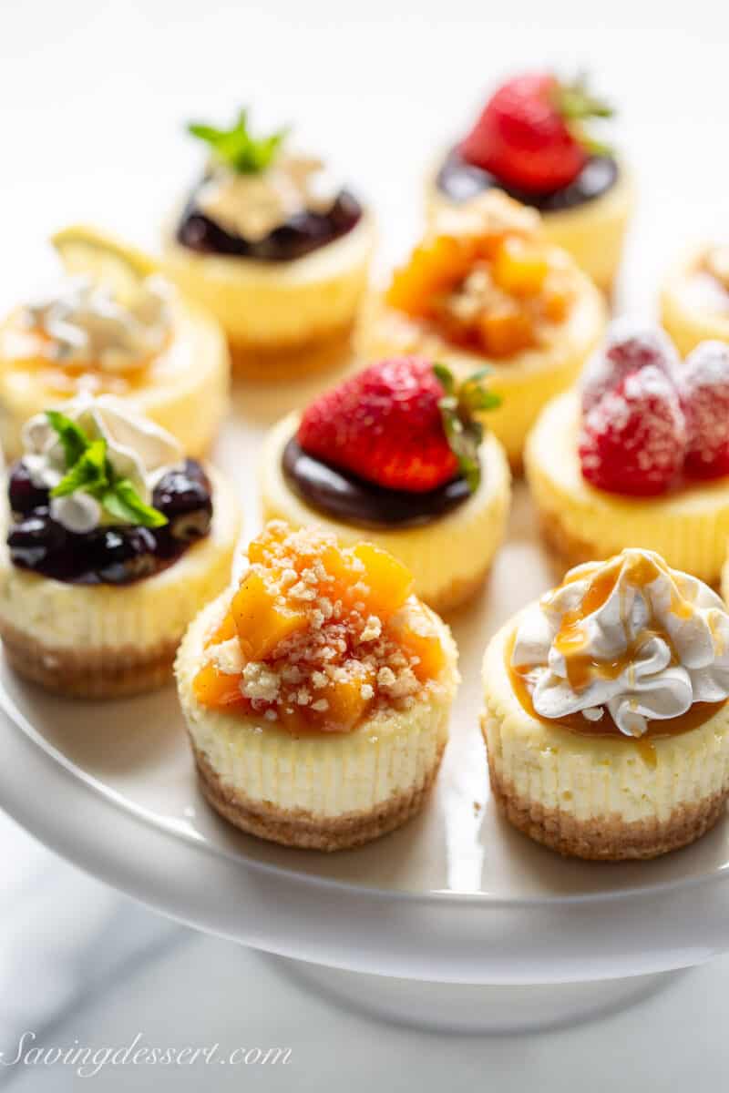 A cake stand holding an assortment of individual mini cheesecake recipe with various toppings