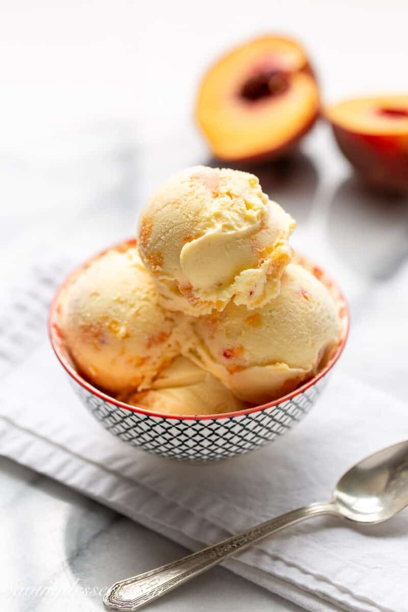 peach ice cream in a bowl with sliced peaches in the background