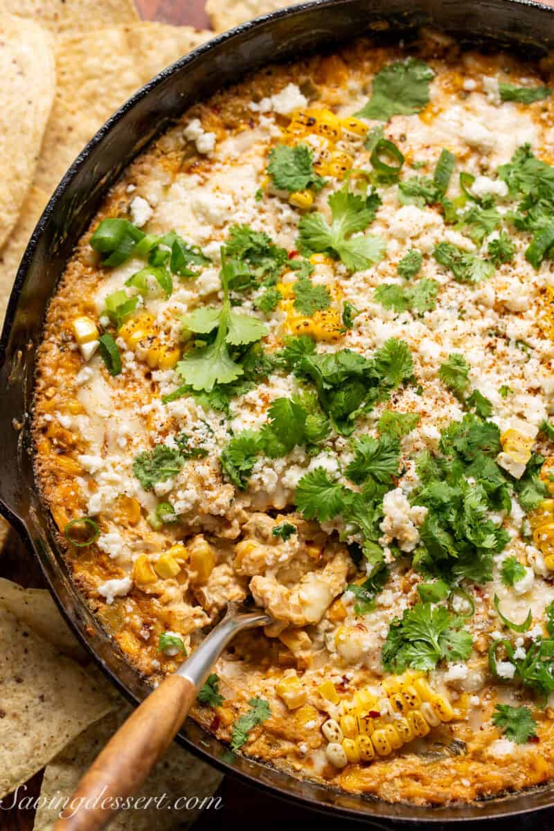 Overhead view of a skillet filled with cheesy corn dip garnished with cilantro and cotija cheese