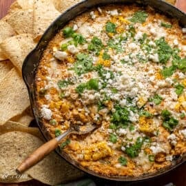 Overhead shot of a skillet filled with corn dip with cheese on top and chips on the side