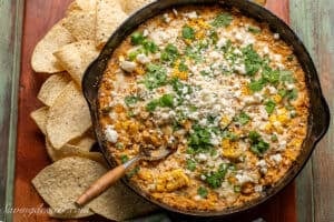 Overhead shot of a skillet filled with corn dip with cheese on top and chips on the side