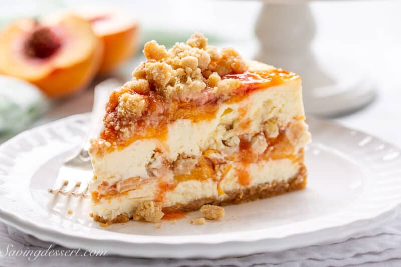 A pretty slice of peach crumble cheesecake with juices dripping down the sides.