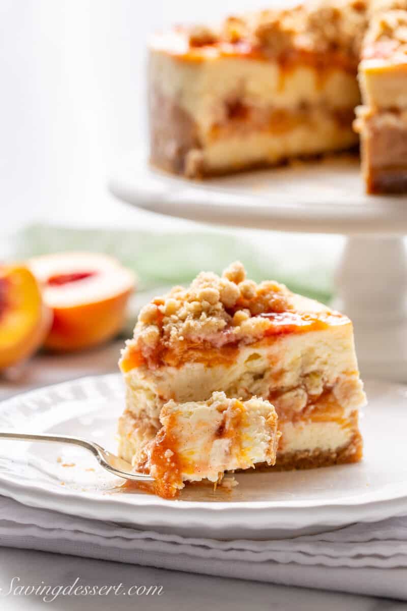 A side view of a slice of peach cobbler cheesecake topped with peaches and a cinnamon crumble topping.