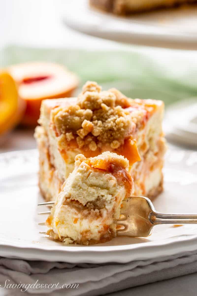 A closeup shot of a slice of peach cobbler cheesecake with a fork cutting off a piece.