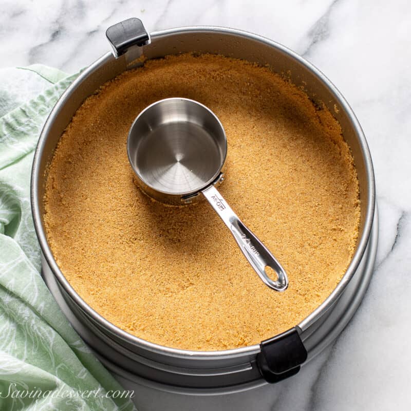 A graham cracker crumb crust being pressed into a springform pan.