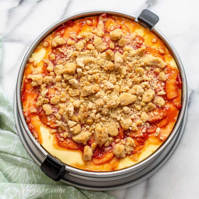 An overhead shot of a peach cheesecake with a crumble top in a springform pan.