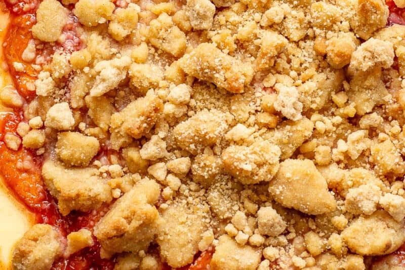 A closeup overhead view of a baked peach crumble cheesecake on a cake platter.