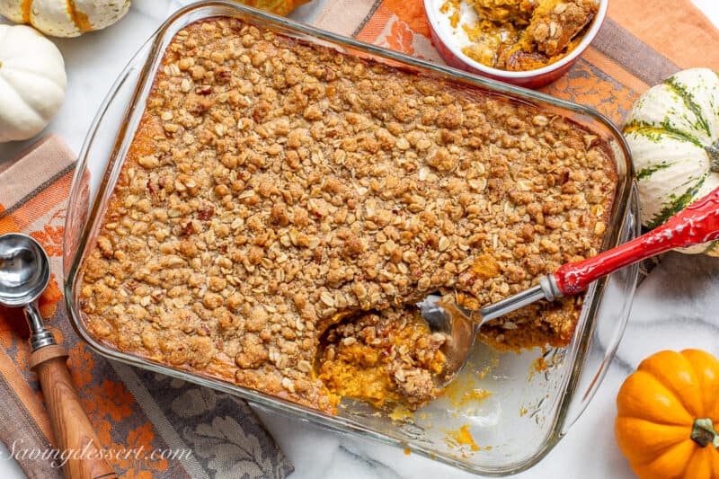 An overhead shot of a pan filled with pumpkin crisp with a bowl on the side.