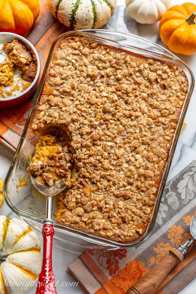 A pan filled with pumpkin crisp with a large spoon scooping out a serving.