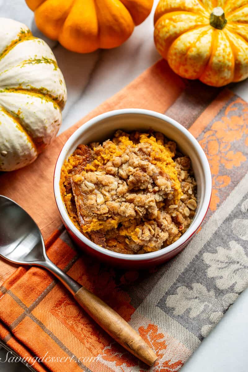 An overhead view of a bowl of pumpkin crisp with mini pumpkins in the background.