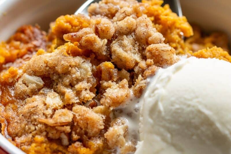 A spoonful of pumpkin crisp being scooped out of a bowl.