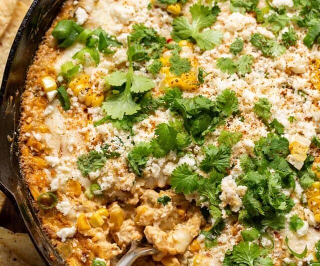 Overhead view of a skillet filled with cheesy corn dip garnished with cilantro and cotija cheese