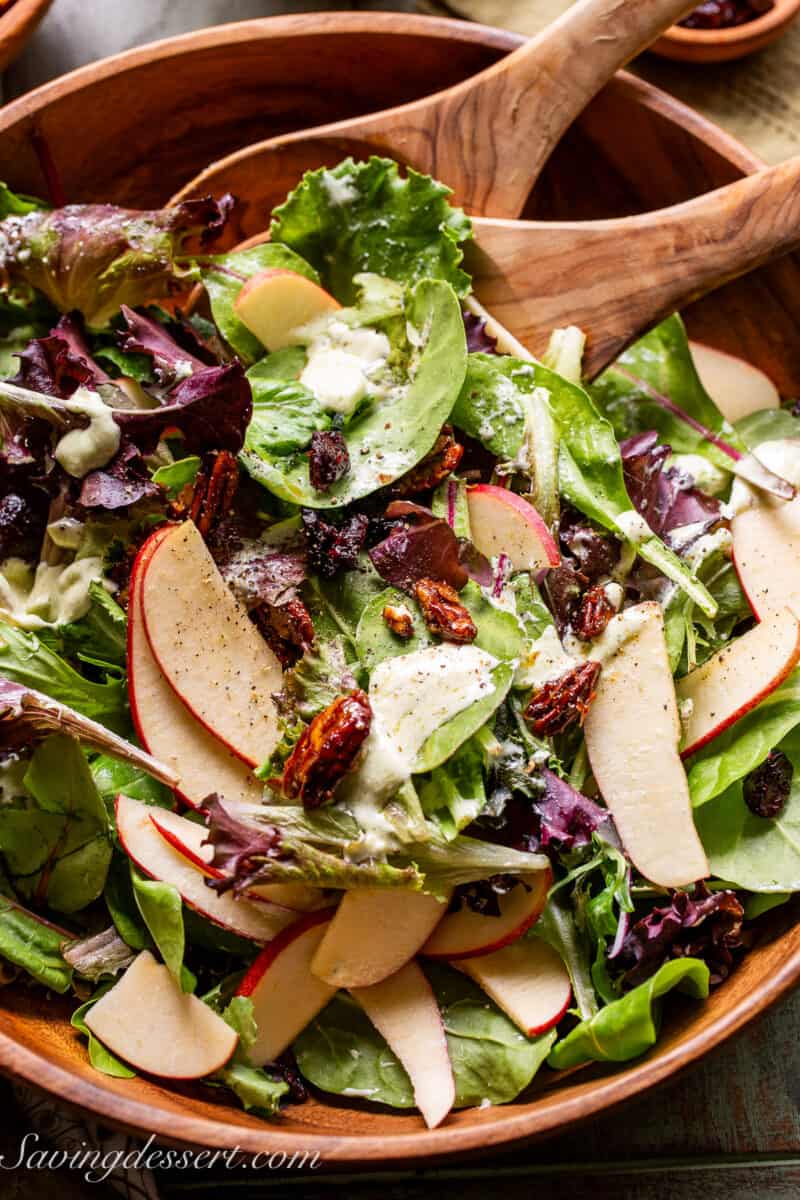 Overhead view of a wooden bowl filled with salad topped with apples, onions and a creamy feta dressing.