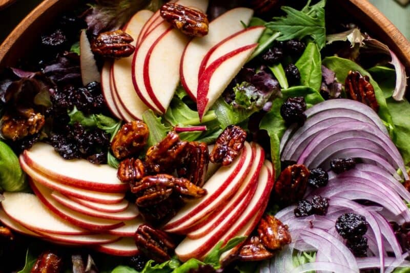 An overhead view of a wooden bowl filled with salad and sliced apples