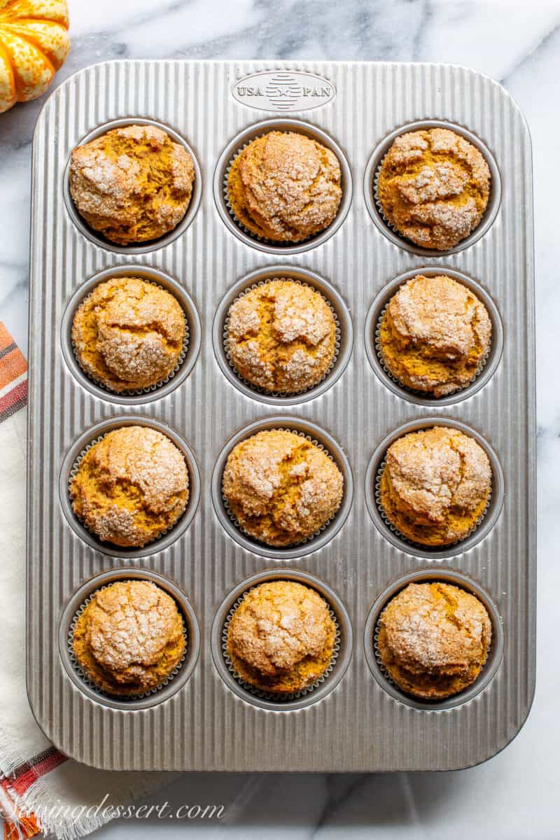 A muffin tin with fresh baked pumpkin muffins with a crusty sugar topping.