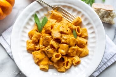 An overhead view of a bowl of pasta with a creamy cheesy pumpkin sauce and fresh sage.