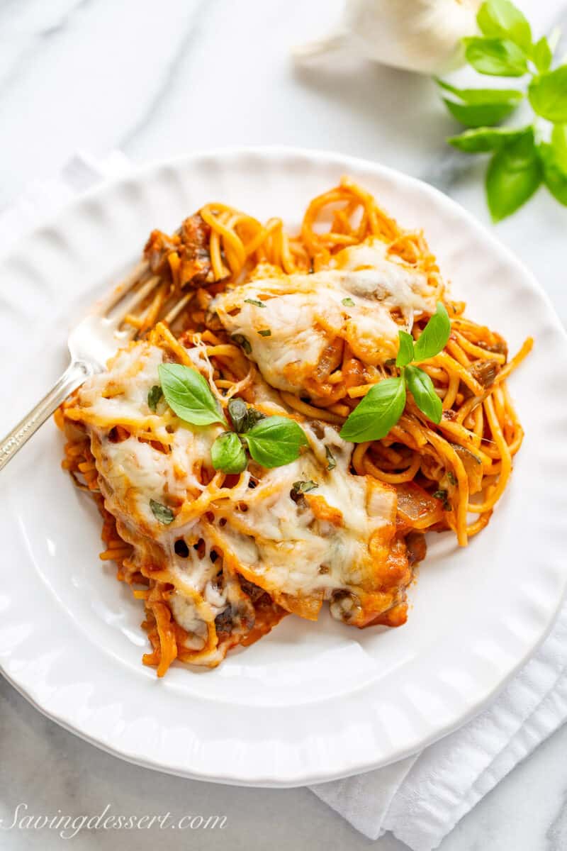 An overhead of a plate with baked spaghetti topped with fresh basil and plenty of cheese.