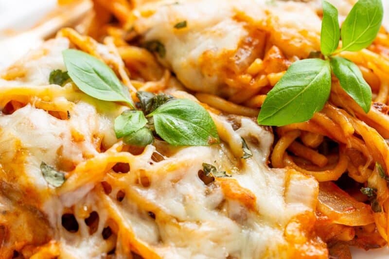 A plate with baked spaghetti loaded with cheese and fresh basil.