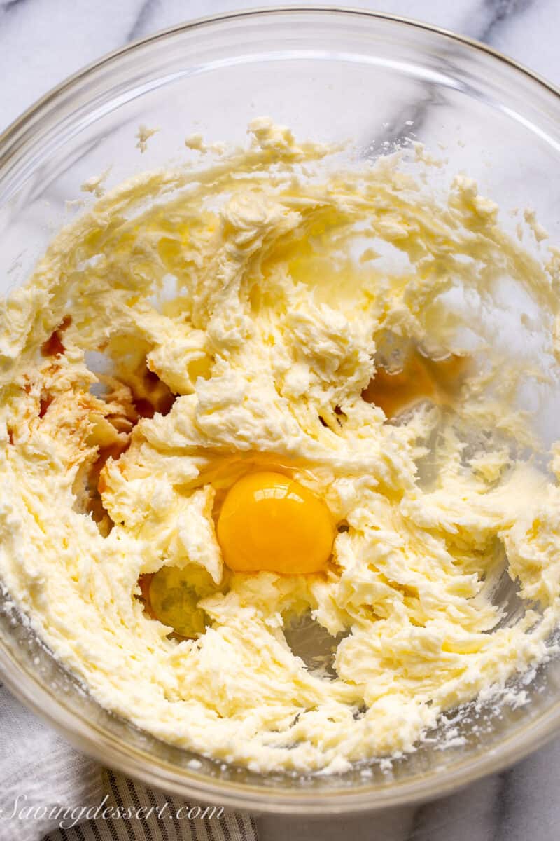 A mixing bowl with creamed butter and sugar with an egg and vanilla ready to blend in.