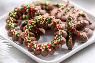 Chocolate Spritz Cookies shaped like holiday wreaths decorated with nonpareils.