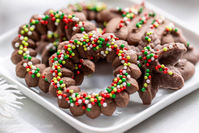 Chocolate Spritz Cookies shaped like holiday wreaths decorated with nonpareils.