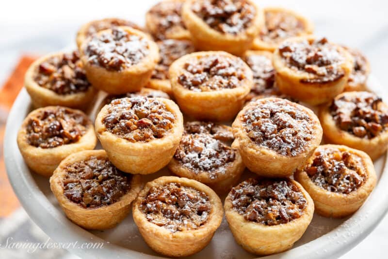 Pecan tassies dusted with powdered sugar on a cake stand.