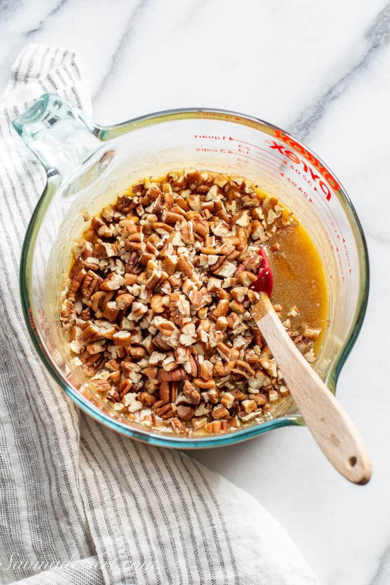 A measuring cup filled with a brown sugar butter mixture along with chopped pecans.