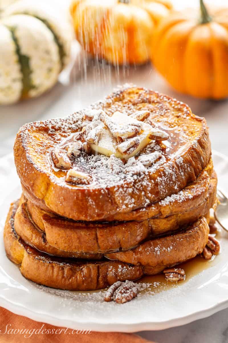 Powdered sugar being sifted over a stack of pumpkin French toasts.