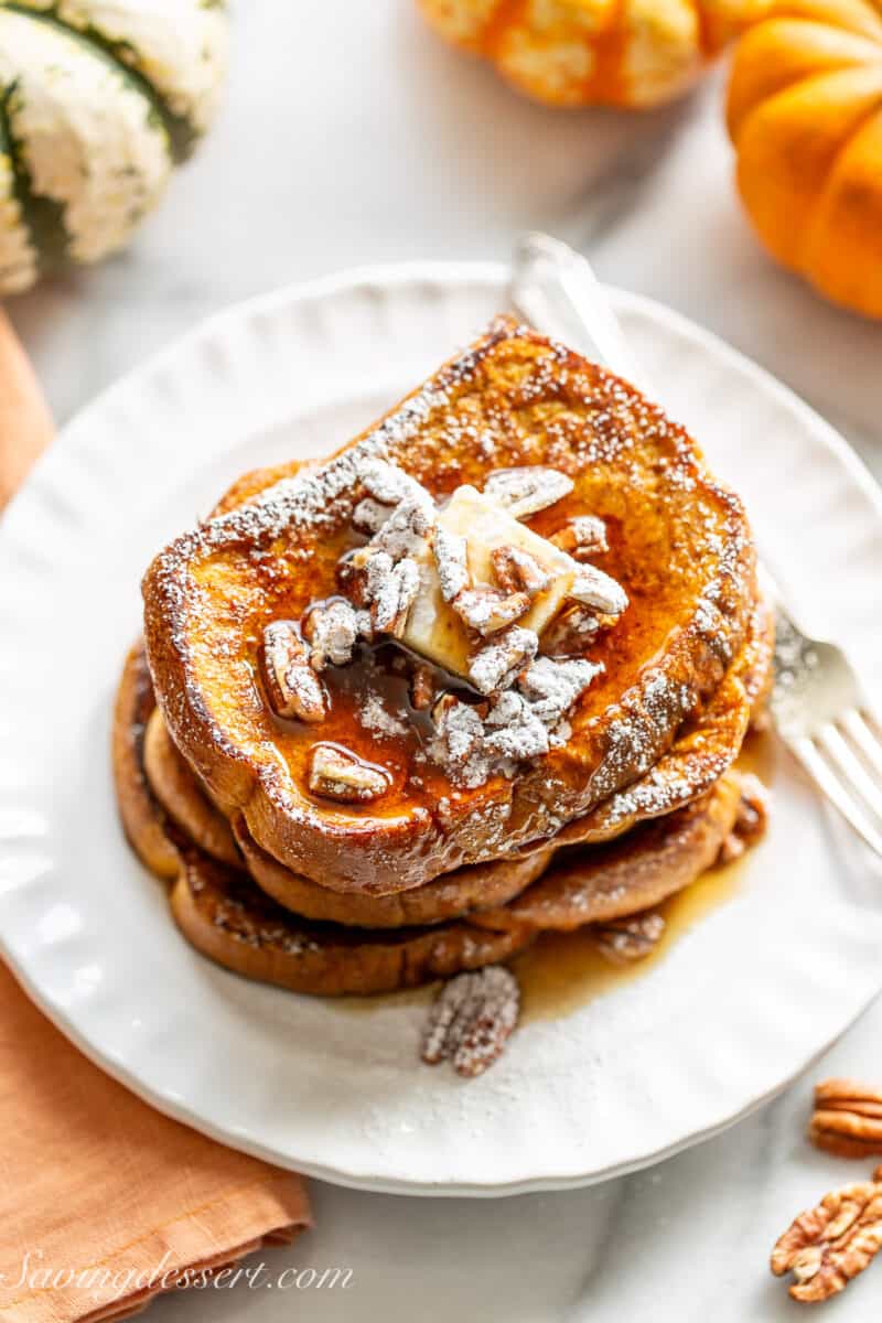 Stack of French toast on a white plate with pecans and syrup.