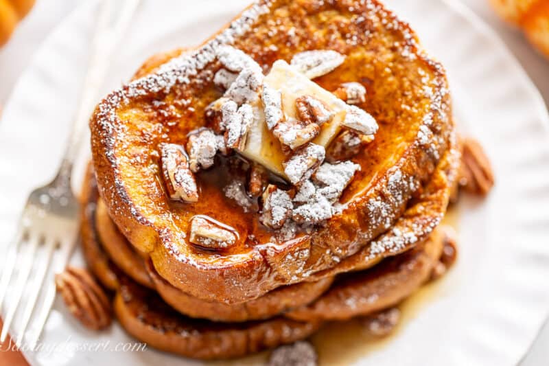 Overhead shot of a stack of pumpkin French toasts on a plate with powdered sugar on top.
