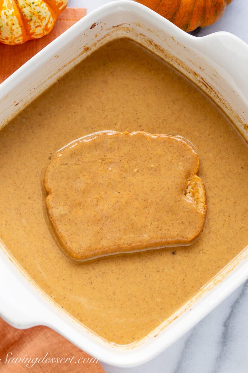 A slice of bread soaked in a dish filled a with Pumpkin French Toast mixture.