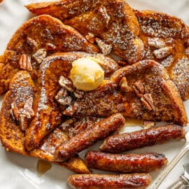 A plate filled with French toast wedges topped with syrup, butter and served with link sausages.