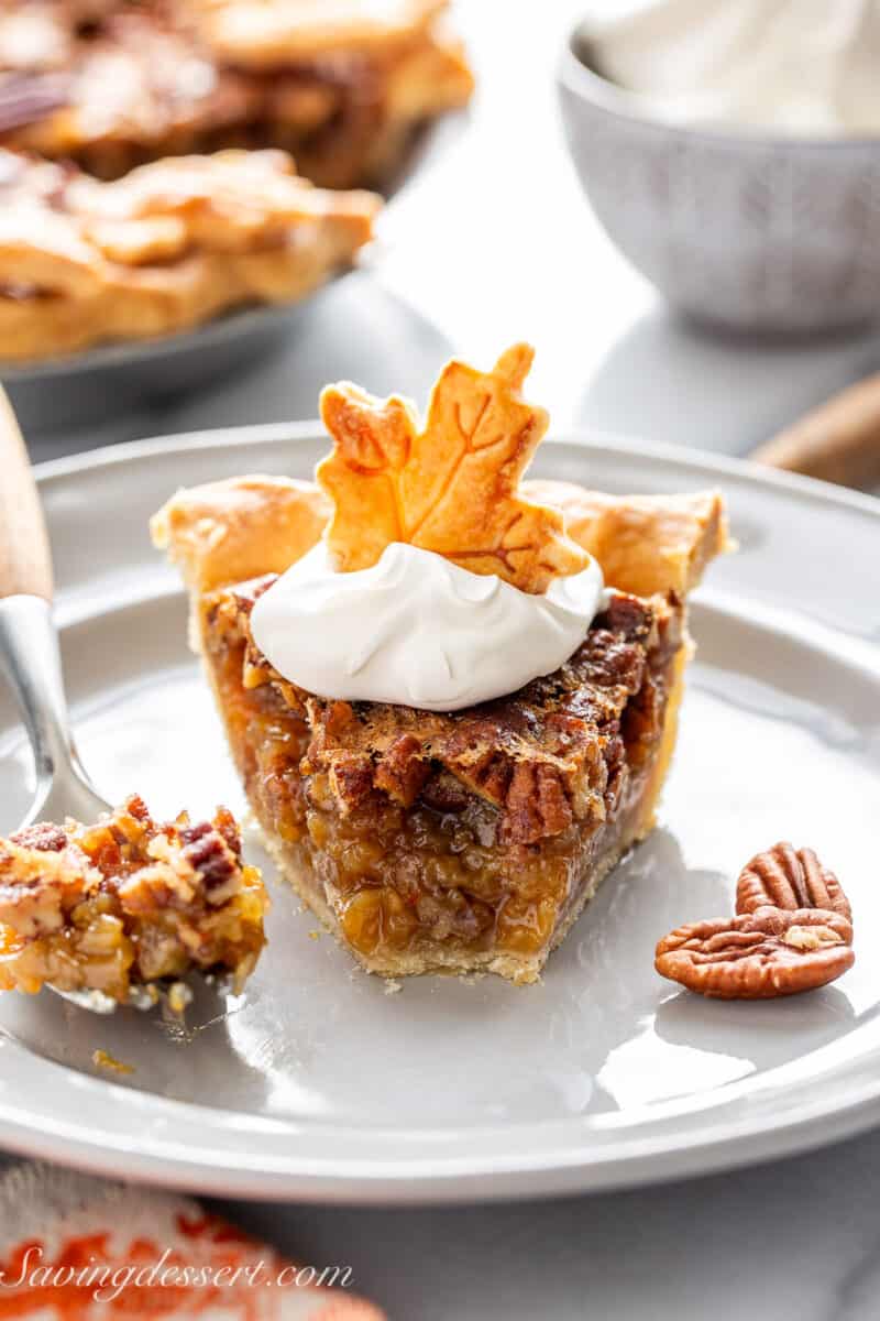 A slice of pecan pie on a plate topped with whipped cream and a leaf cut out crust cookie.