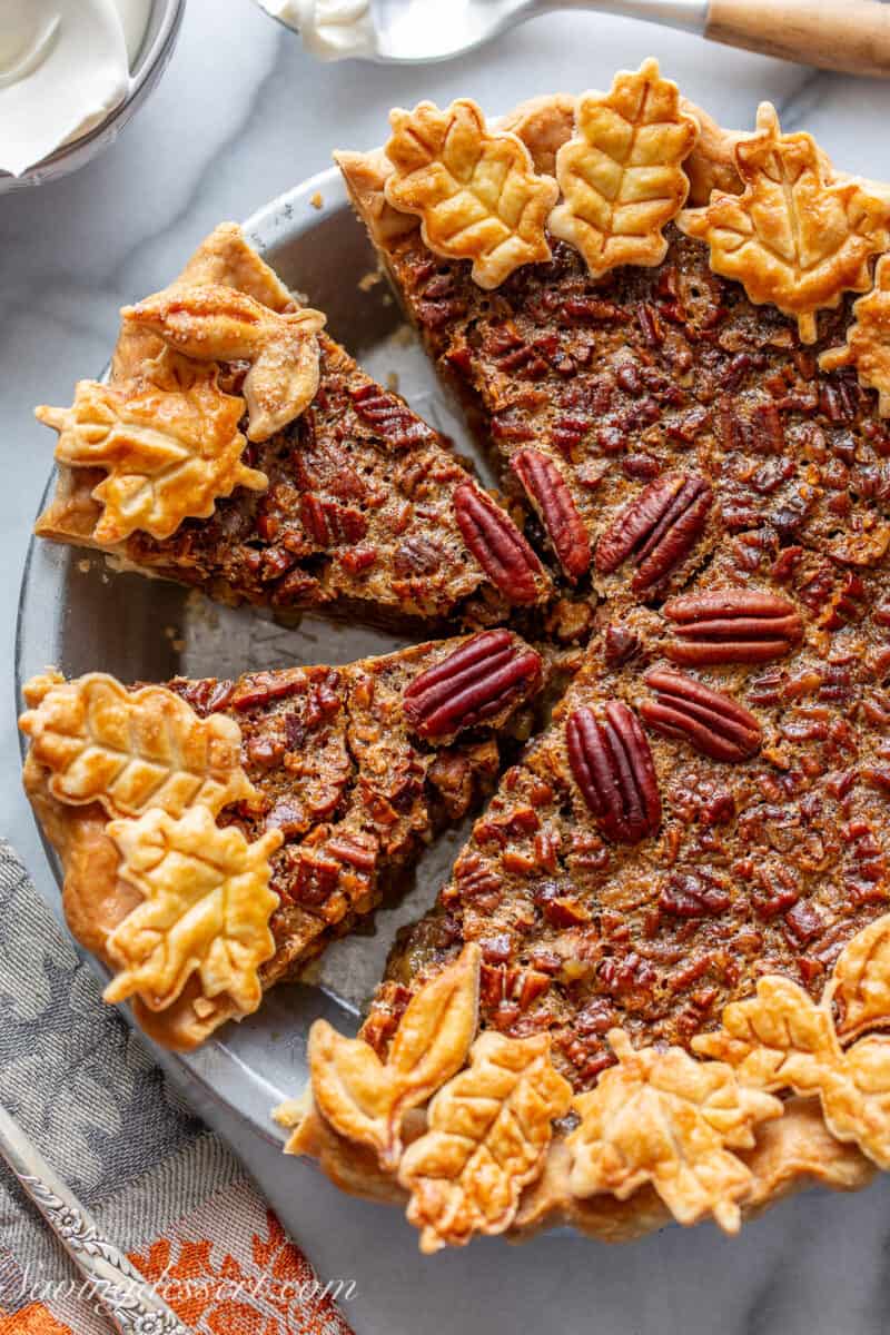 An overhead shot of a sliced pecan pie decorated with leaves cut out of pastry crust and baked until golden brown.