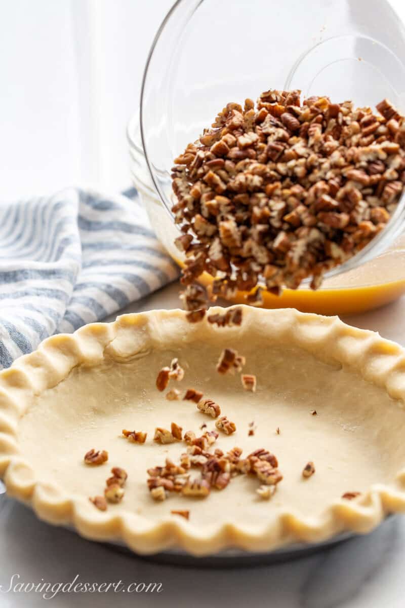 Chopped pecans being poured into an unbaked pie crust.