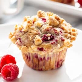 A raspberry muffin with a streusel topping on a plate with fresh raspberries.