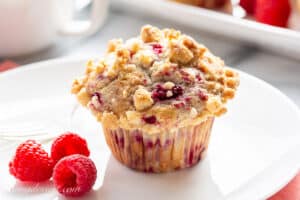 A raspberry muffin with a streusel topping on a plate with fresh raspberries.