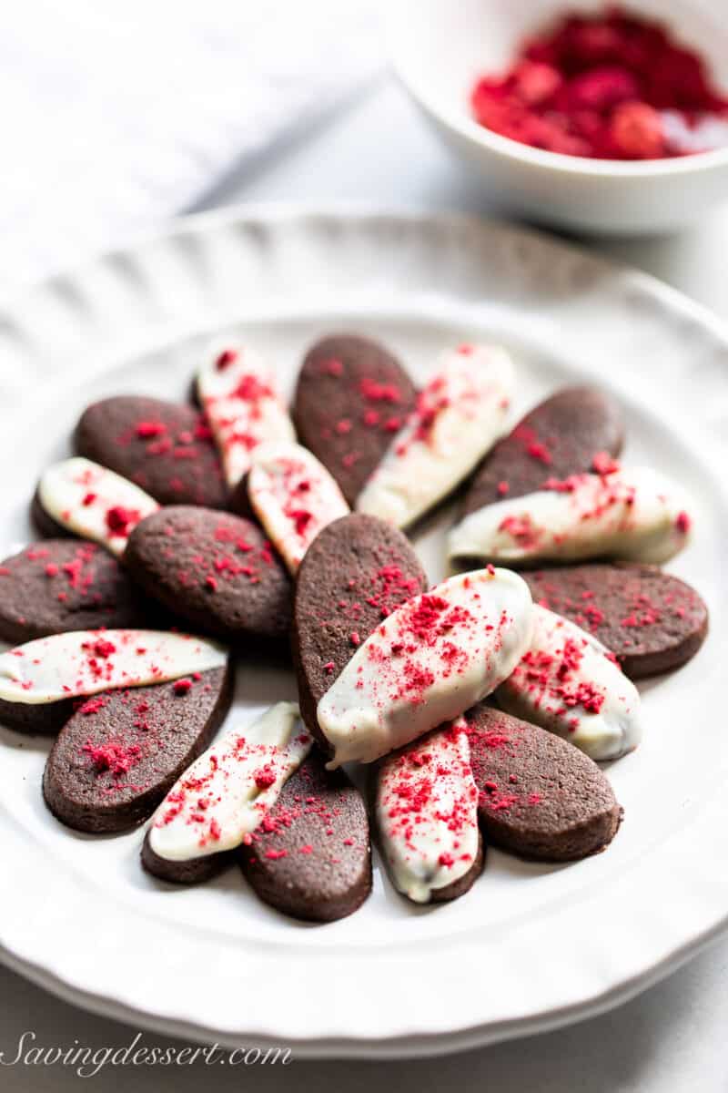A plate filled with mini chocolate heart shaped cookies dipped in white chocolate.